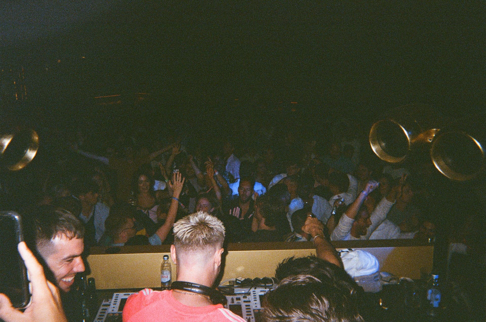 DJs at the decks in front of a packed, dancing crowd, shot on film